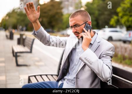 Porträt eines frustrierten Geschäftsmannes, der telefoniert. Mann, der in der Stadt auf der Bank sitzt und telefoniert. Stockfoto