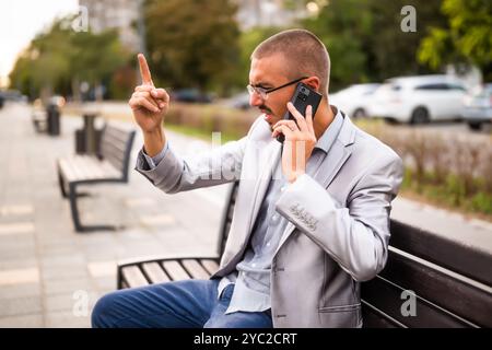 Porträt eines frustrierten Geschäftsmannes, der telefoniert. Mann, der in der Stadt auf der Bank sitzt und telefoniert. Stockfoto