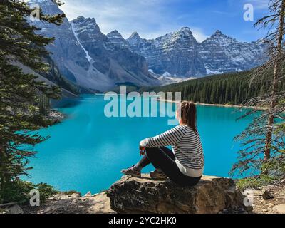 Frau, die auf einem Felsen sitzt und den türkisfarbenen Moraine Lake in Banff überblickt. Stockfoto