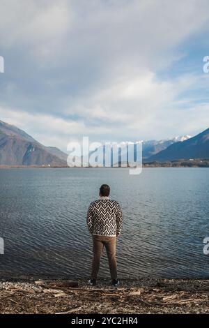 Stilvoller junger Mann, der vor Bergen und See steht Stockfoto