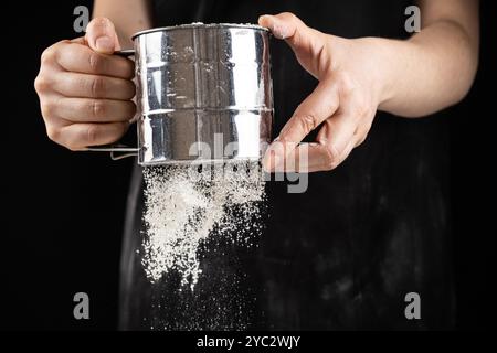 Der Koch siebt das Weizenmehl durch ein Metallsieb Stockfoto