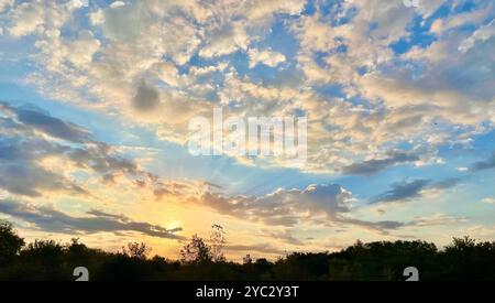 Majestätischer Sonnenaufgang färbt den Himmel in Gold- und Blautönen. Wolken fangen das auftauchende Licht über einer Silhouette ein. Stockfoto