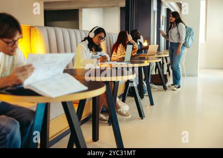 Eine vielfältige Gruppe von Schülern studiert in einem modernen Schulflur mit Laptops und Büchern und symbolisiert Konzentration und Teamarbeit in einer lernumgebung Stockfoto