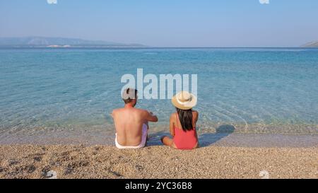 Ein Paar genießt die Ruhe des klaren blauen Wassers von Brac Island, das Seite an Seite am Sandstrand sitzt. Die Sonne taucht sie in Wärme, während sie soa Stockfoto