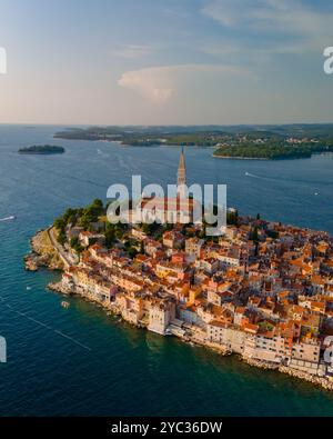 Goldene Farbtöne tauchen über Rovinj, während die Sonne untergeht und farbenfrohe Häuser an der Küste beleuchtet, während die historische Kirche hoch steht und ein Bild schafft Stockfoto