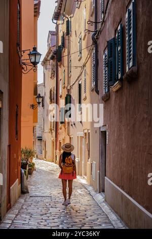 Ein Reisender schlendert durch eine enge Kopfsteinpflasterallee in Rovinj, Kroatien, umgeben von bunten Gebäuden und Vintage-Laternen, die sich in der warmen L Stockfoto