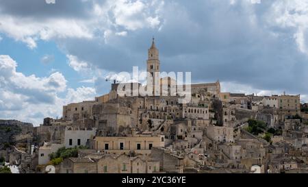 Eingebettet im Herzen von Apulien besticht Matera mit seinen alten Steinbauten und hoch aufragenden Kirchen, die wunderschön vor einem dramatischen Himmel beleuchtet sind und einen zeitlosen italienischen Charme verkörpern. Stockfoto