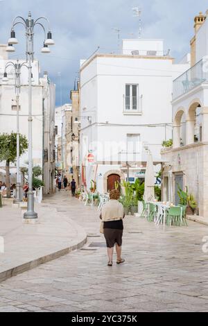 Ostuni Italien am 18. September 2024 wandert Eine einsame Figur durch die ruhigen Straßen Apuliens, umgeben von malerischen Gebäuden und einladenden Cafés. Die Atmosphäre Stockfoto