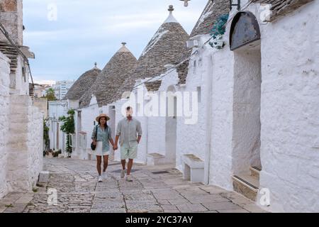 Ein paar Spaziergänge Hand in Hand entlang der kopfsteingepflasterten Straßen von Alberobello Italien, umgeben von berühmten Trullihäusern. Das warme Abendlicht fügt einen roma hinzu Stockfoto