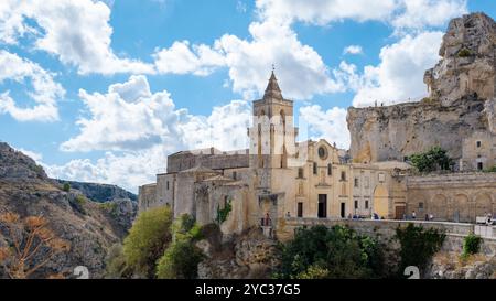 Im Herzen von Matera, Apulien, Italien, erheben sich die alten Steinbauten majestätisch, eingerahmt von einem strahlend blauen Himmel und geschwollenen Wolken. Die reiche Geschichte fügt sich nahtlos in die atemberaubende Landschaft ein. Stockfoto