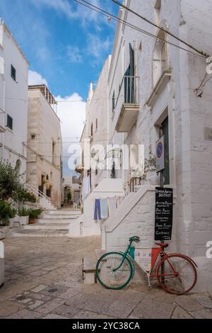 Ostuni Italien 18 September 2024 Eine malerische Gasse in Apulien, Italien, bietet charmante weiß getünchte Gebäude mit lebhafter Wäscherei. Eine rote und grüne Bizie Stockfoto