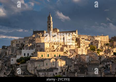 Goldenes Licht taucht die historischen Höhlenhäuser von Matera, während die Sonne hinter der mittelalterlichen Architektur untergeht. Diese bezaubernde Landschaft fängt die ess ein Stockfoto