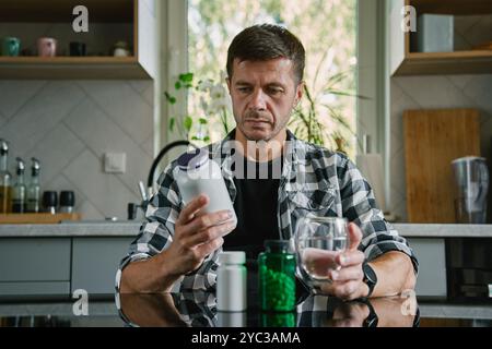 Der Mann sitzt am Tisch in der Küche und sieht sich verschiedene Flaschen mit Medikamenten-Kapseln an. Die Person nimmt Pillen oder Vitamine ein. Das Konzept der Nahrungsergänzungsmittel, medici Stockfoto