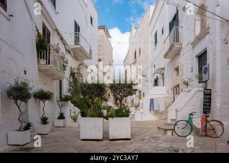 Ostuni Italy 18 September 2024, Eine charmante Gasse in Apulien, Italien, zeigt weiß getünchte Gebäude neben grünen Pflanzgefäßen, während die Kleidung in der Sonne trocknet Stockfoto