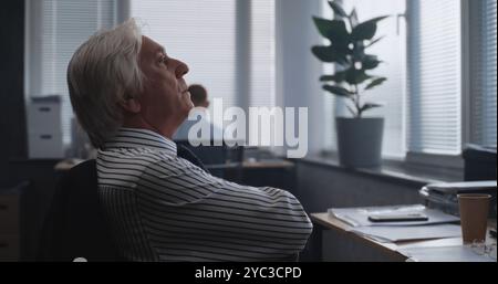 Müde Senior Financial Specialist analysiert Papiere und Dokumente, überwacht Börsen und Aktien am Computer. Der professionelle Händler arbeitet im modernen Büro der internationalen Börsengesellschaft. Stockfoto