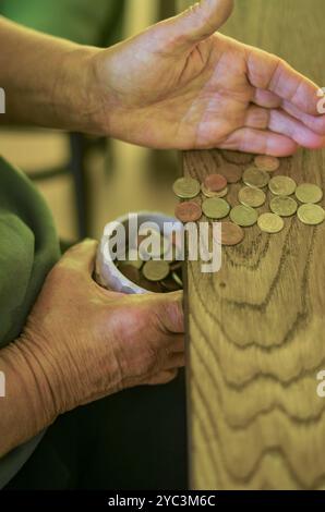 Seniorhände für Erwachsene sortieren kleine Wechselgeld in einen Behälter auf einem Holztisch. Hochwertige Fotos Stockfoto