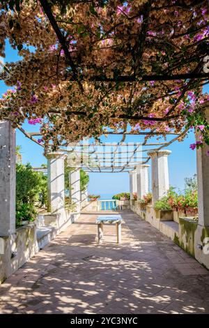 Eingebettet an der atemberaubenden Amalfiküste erwartet Sie eine ruhige Terrasse, eingerahmt von lebhaften Bougainvillea. Ein einfacher Tisch lädt zu Momenten der Reflexion bei atemberaubendem Blick auf die Küste ein. Ravello Italien Stockfoto