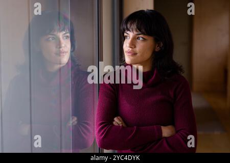 Frau in einem gemütlichen Pullover, der zu Hause nachdenklich aus dem Fenster schaut Stockfoto