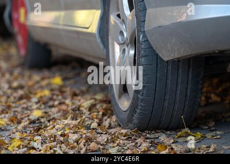 Ein silbernes Auto mit einem Platten Reifen ist umgeben von herabfallenden Herbstlaub auf dem Boden. Stockfoto