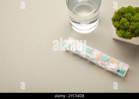 Pillenbox mit Medikamenten und Glas Wasser auf grauem Hintergrund. Leerzeichen für Text. Draufsicht Stockfoto