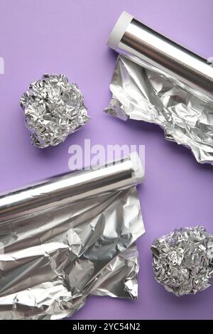 Rollen aus Aluminiumfolie auf violettem Hintergrund. Vertikales Foto. Draufsicht Stockfoto