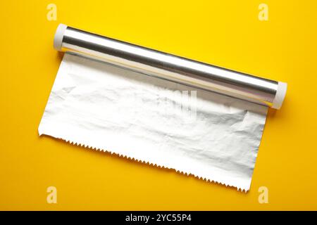 Rolle Aluminiumfolie auf gelbem Hintergrund. Draufsicht Stockfoto