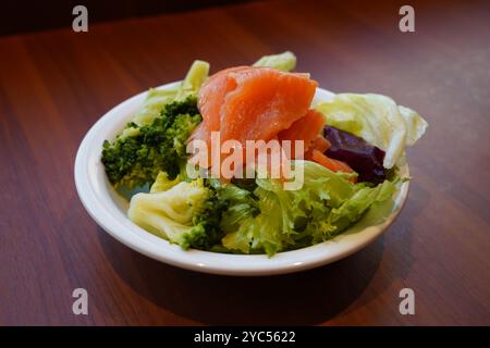 Salat mit Lachs und Brokkoli auf weißem Teller auf Holztisch Stockfoto