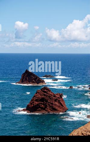 Rötliche vulkanische Felsen, die aus dem tiefblauen Atlantik nahe der Küste von Vereda da Ponta de São Lourenco hervorgehen Stockfoto
