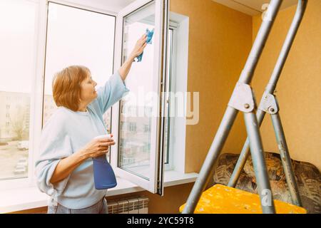 Reinigungsappartement Für Ältere Frauen. Active Seniors-Konzept. Glückliche Schüchterne, Fröhlich Lächelnde Reife Frau, Die Das Fenster Reinigt. Kaukasische Frau Im Mittleren Alter Stockfoto
