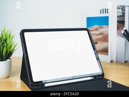 Tablet mit leerem Bildschirm auf Holztisch. Bürobedarf, Bücher, Zimmerpflanzen, auf Holztisch und weißer Wand. Platz zum Kopieren Ihres Textes, Workspac Stockfoto