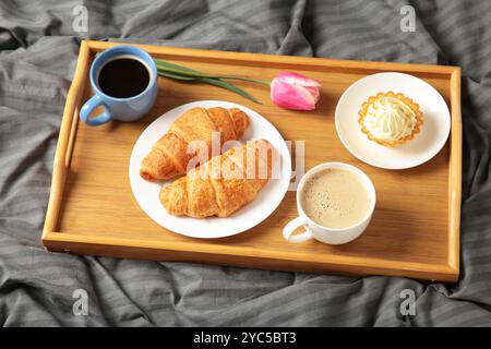 Frühstück im Bett mit Kaffee, Croissants und Tulpe auf Tablett. Draufsicht Stockfoto
