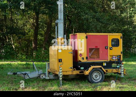 Auf einer von Bäumen umgebenen Rodung steht ein mobiler Generator, der bei Tageslicht Strom für Bauarbeiten liefert. Die Ausrüstung ist bereit für Stockfoto