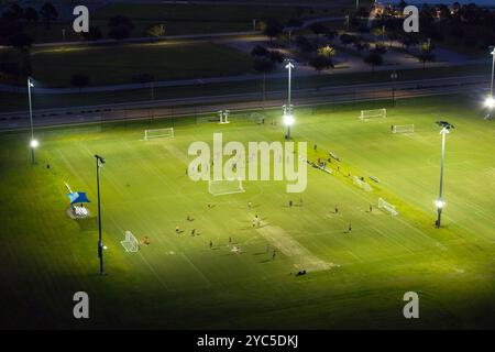 Blick aus der Vogelperspektive auf den öffentlichen Sportpark mit Menschen, die bei Sonnenuntergang im Grasstadion spielen. Aktives Lebenskonzept. Stockfoto