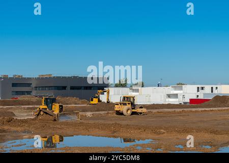 Schwere Maschinen werden auf einer Baustelle eingesetzt, bewegen die Erde und bereiten den Boden für zukünftige Entwicklungen unter klarem blauem Himmel vor. Die Gegend ist Bus Stockfoto