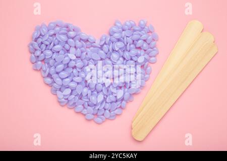 Holzstäbchen für Wachs und Spa mit Wachsgranulat in Form eines violetten Herzens auf rosa Hintergrund. Draufsicht. Stockfoto