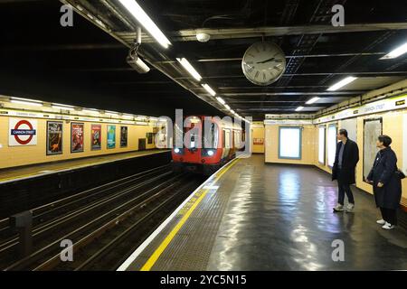 London, England, Großbritannien - zwei Personen auf dem Bahnsteig beobachten einen U-Bahn-Zug der District Line zum Ealing Broadway, der an der U-Bahn-Station Cannon Street ankommt Stockfoto