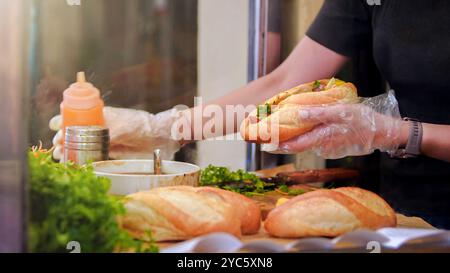 Der Koch serviert das typische Banh Mi, ein vietnamesisches Sandwich mit einer Mischung aus Fleisch und Gemüse. Dieses kurze Baguette ist vollgepackt mit Fleisch und herzhaften Zutaten Stockfoto