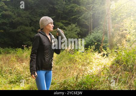 Sportliche Frau, die nach dem Training und Joggen im Freien in der herbstlichen Landschaft Wasser aus einer Flasche trinkt Stockfoto