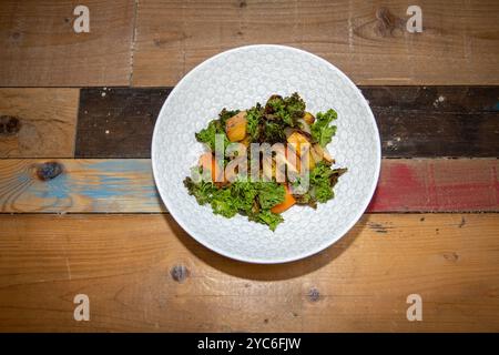 Ein köstlicher Teller mit gebratenen Wurzeln mit Apfelkohl und Crispy Seeds auf einem hölzernen Küchentisch oder einer Arbeitsplatte Stockfoto