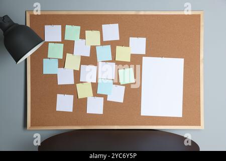 Korkbrett mit leeren Notizen, Lampe und grauer Wand des schwarzen Tisches Stockfoto
