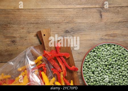 Gefrorene grüne Erbsen in der Schüssel und Paprika auf Holztisch, Blick von oben Stockfoto