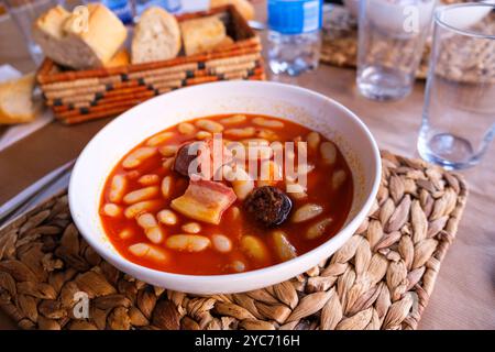 Eine Schüssel mit Fabada asturiana, einem traditionellen spanischen Eintopf aus Bohnen und verschiedenen Fleischgerichten, steht auf einem Holztisch. Stockfoto