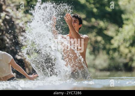 Junger Mann spritzt freudig Wasser in einer sonnigen Umgebung im Freien Stockfoto