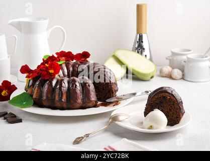 Schokoladenkuchen Brownie mit Zucchini dekoriert mit Kapuzinerkuchen-Blüten auf weißer Platte auf weißem Hintergrund mit Schnittstück auf der Platte mit Eis Stockfoto