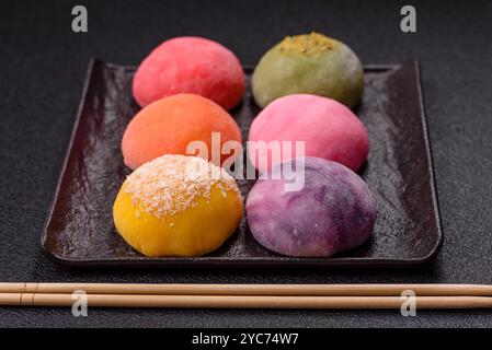 Köstliche bunte asiatische Mochi-Süßigkeiten mit Reisteigschale und Fruchtfüllung auf dunklem Betonhintergrund Stockfoto