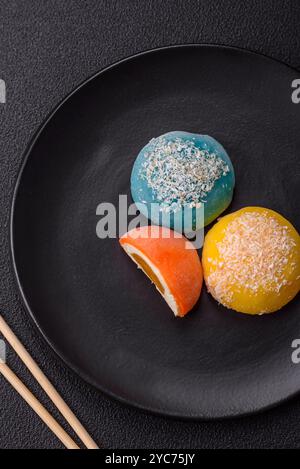 Köstliche bunte asiatische Mochi-Süßigkeiten mit Reisteigschale und Fruchtfüllung auf dunklem Betonhintergrund Stockfoto