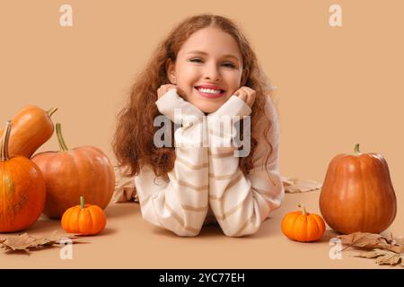 Junge Frau mit Kürbissen und Herbstblättern auf beigefarbenem Hintergrund Stockfoto