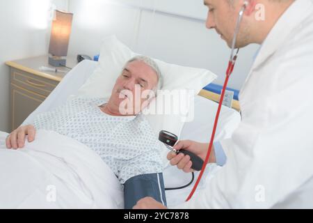 Männlicher Arzt überprüft Senioren-bemannt Blutdruck im Krankenhaus Stockfoto