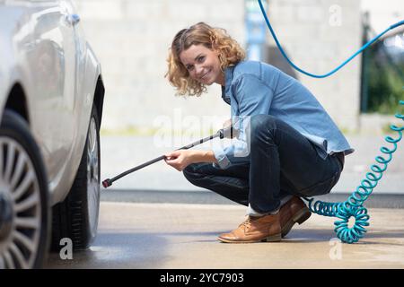 Eine junge Frau wäscht ihr Auto mit Hochdruckwasser Stockfoto