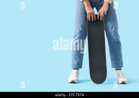 Junger Mann in Turnschuhen mit Skateboard auf blauem Hintergrund Stockfoto